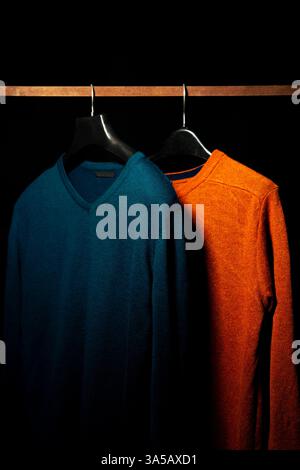 Immagine dettagliata di una semplice felpa arancione e verde acqua appesa su un gancio su uno sfondo nero. Ideale per mostrare i dettagli dell'abbigliamento Foto Stock