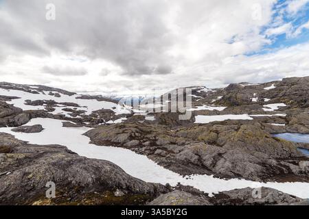 Splendida vista panoramica su terreni accidentati con affioramenti rocciosi e macchie di neve, sotto un cielo spettacolare pieno di nuvole, che ne mostra la bellezza Foto Stock