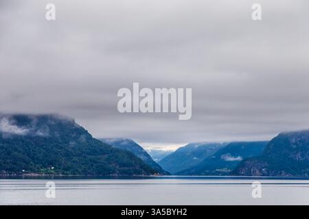 Maestoso fiordo norvegese: Un affascinante paesaggio sotto i cieli grigi che cattura la tranquillità e la grandezza della natura in una scena costiera mistica dal Foto Stock