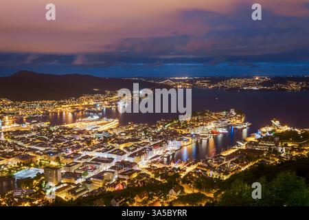 Splendida vista aerea sul vibrante paesaggio urbano di Bergen, Norvegia, che mostra il suo porto panoramico e gli edifici illuminati contro il cielo crepuscolo Foto Stock