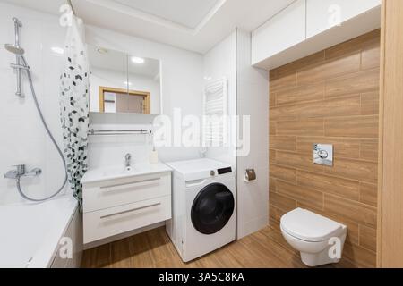 Gli interni luminosi e contemporanei dei bagni presentano una lavatrice, eleganti pannelli in legno e elementi bianchi incontaminati, adatti per livi moderni Foto Stock