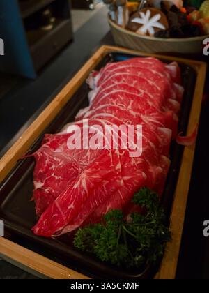 Manzo crudo a fette sottili in un vassoio, pronto per essere cucinato in una pentola calda, un pasto di cucina asiatica. Foto Stock