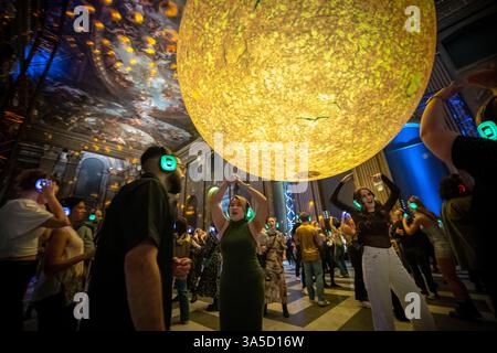Londra, Regno Unito. 22 marzo 2025. Silent disco sotto «Helios», la nuova installazione artistica del sole di Luke Jerram nella Painted Hall, Old Royal Naval College, Greenwich. Sabato sera abbiamo visto una discoteca silenziosa come nessun'altra con ballerini riuniti nell'iconica sala dipinta, mentre veniva trasformata in una luminosa pista da ballo dove arte, musica e atmosfera si combinavano per una notte indimenticabile. Crediti: Guy Corbishley/Alamy Live News Foto Stock