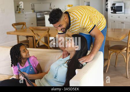 Padre sorridente mentre parla con la figlia e la madre che si rilassano sul divano di casa Foto Stock