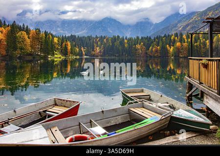 L'attracco delle barche. Il Lago Fusine in Italia. I colori vivaci delle foreste autunnali si riflettono nelle acque ghiacciate del lago. Montagne ricoperte di mora Foto Stock