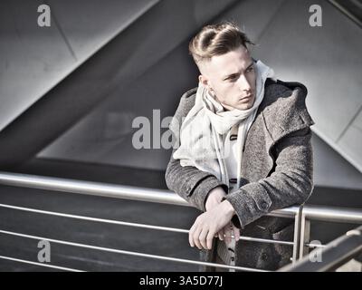 Un bel giovane uomo nel contesto urbano in moden city, in piedi, indossando il manto nero e sciarpa in giornata invernale Foto Stock
