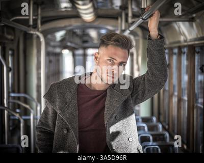 Giovane uomo bello a cavallo su tram o bus vecchio in città, indossare abbigliamento invernale Foto Stock