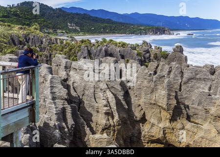 Piattaforma di osservazione. La donna scatta foto di rocce e surf oceanico. Nuova Zelanda. Sassi i pancake piatti, impilati uno sopra l'altro. Il concetto di ecologi Foto Stock