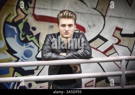 Bello dai capelli biondi giovane uomo appoggiato sulla ringhiera di metallo, in ambiente urbano Foto Stock