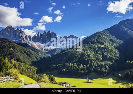 Pittoresca chiesetta di Santa Maddalena nella Val di Funes. Cime rocciose e montagne boscose circondate da verdi prati alpini. Giornata di sole Foto Stock