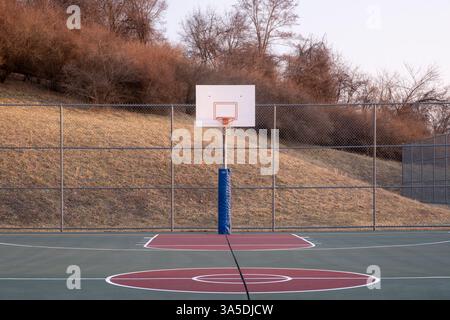 Il campo da pallacanestro vuoto mette in mostra un cerchio contro una collina marrone al crepuscolo Foto Stock