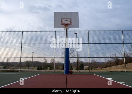 Un canestro da basket si erge in modo prominente su un campo circondato da alberi e da un cielo nuvoloso. Foto Stock