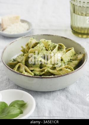 Primo piano di pasta verde, tagliatelle al pesto con foglie di basilico e parmigiano. Cucina tradizionale italiana Foto Stock
