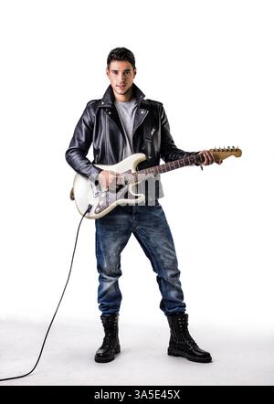 Ritratto a tutta lunghezza di un giovane uomo che indossa una giacca in pelle e stivali da combattimento che suonano la chitarra elettrica in Studio con sfondo bianco Foto Stock