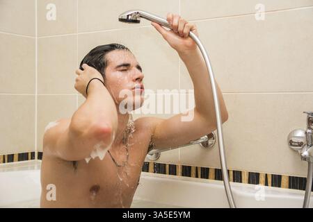 Bel giovane nella vasca da bagno a casa avente vasca, lavaggio del corpo e dei capelli con il Bagnoschiuma e shampoo Foto Stock