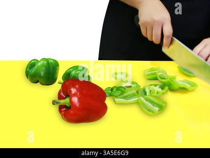 Tagliate a pezzi di peperoni freschi in rosso e verde su un tagliere verde su bianco isolato. Foto Stock