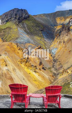Montagne multicolore di riolite minerale sono illuminate dal sole. Due chaise longue rosse collegate da un piccolo tavolo per i turisti Foto Stock