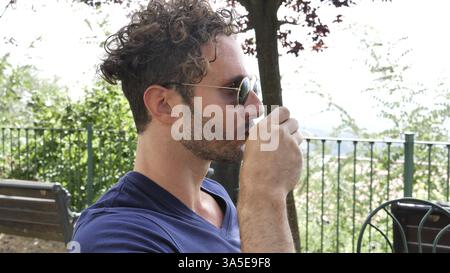 Ritratto di un bel sorridente uomo seduto a tavola con una tazza di caffè, all'aperto sulla caffetteria o sulla terrazza del ristorante, guardando dritto Foto Stock