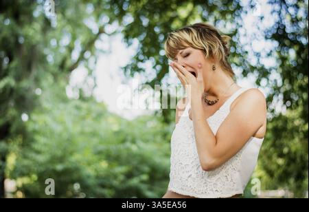 Annoiato o stanco giovane donna in un parco a sbadigliare, che copre la bocca con la mano Foto Stock