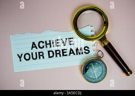 Realizza il testo dei tuoi sogni scritto su carta con bussola e lente d'ingrandimento piatta su sfondo rosa Foto Stock