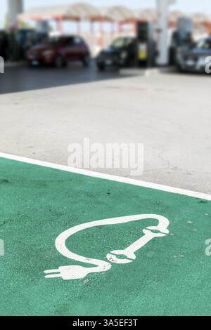 Stazione di ricarica elettrica. Simbolo di ricarica per auto dipinto su asfalto e molte auto sullo sfondo. Concetto di ecologia fuell Foto Stock