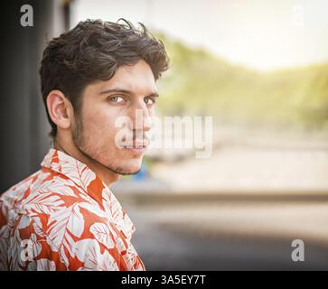 Foto alla testa di un bel giovane con occhi verdi in un ambiente urbano, che guarda la macchina fotografica, indossa una camicia Foto Stock