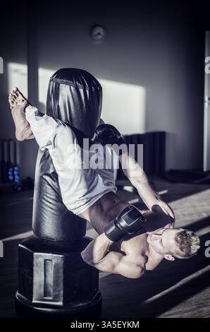 Giovane uomo che lavora in palestra, esercitando abs appesi da boxe Accessori, un sacco da boxe Foto Stock