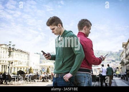 Un paio di uomini, uno accanto all'altro, uno dietro l'altro, coinvolti nei loro cellulari e ignorati la compagnia dell'altro Foto Stock