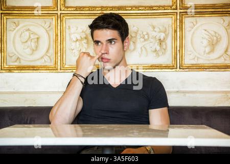 Testa e spalle dell'attraente giovane uomo che raccoglie il naso con le dita di Pinky in camera decorata con marmo bianco e opere d'arte incorniciate in oro Foto Stock