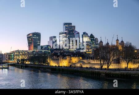 Lo skyline del distretto finanziario della City di Londra e la fortezza illuminata del Tower di Londra lungo il Tamigi al crepuscolo, Inghilterra, Regno Unito Foto Stock