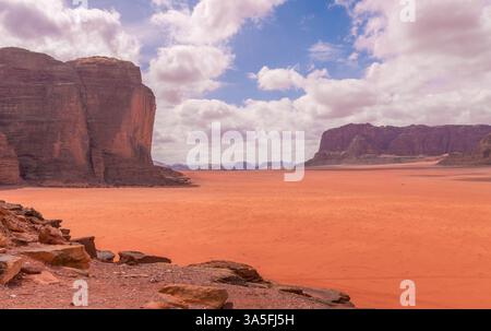 Una splendida vista di Wadi Rum, Giordania, caratterizzata da spettacolari scogliere di arenaria rossa, ampie dune del deserto e un cielo vibrante e nuvoloso. Foto Stock