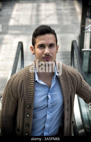 Ritratto di attraente giovane uomo su scale mobili, guardando la fotocamera Foto Stock