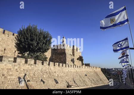 Antica holyJerusalem è la capitale di Israele. Le potenti mura protettive della città vecchia di Gerusalemme al tramonto. Bandiere di Israele che volano su bandiere Foto Stock