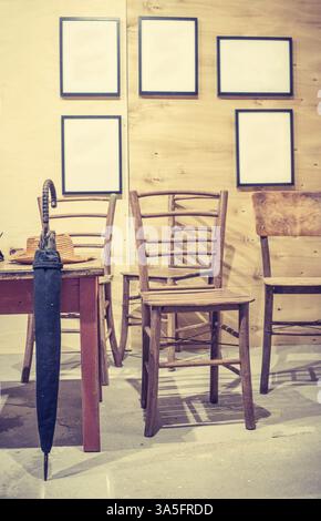 Interni e arredi vintage. Tavolo e sedie vecchi, ombrellone e cappello sul tavolo. Cornici su parete vintage. Toni pastello Foto Stock