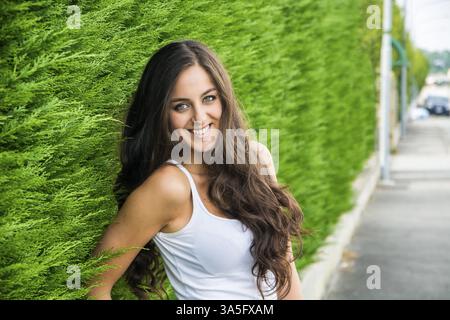 Una donna in piedi di fronte a un cespuglio verde, sorridente alla telecamera Foto Stock
