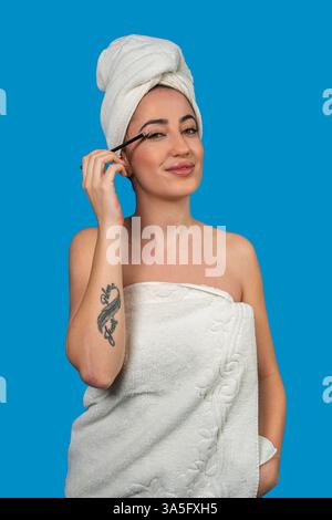 Giovane donna che indossa un asciugamano applicando il mascara dopo una doccia Foto Stock