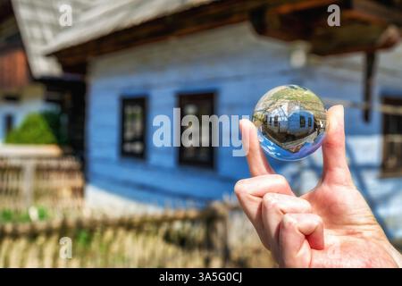 Sfera con lenti di cristallo e vecchia casa rurale nel musem del villaggio slovacco. Architettura popolare Foto Stock