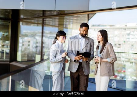 Tre colleghi si riuniscono in un ufficio luminoso, partecipando a una discussione mentre esaminano un tablet insieme. L'atmosfera è piena di creatività Foto Stock