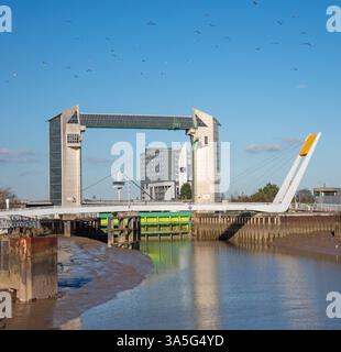 Le torri gemelle hanno una barriera mareale e di fronte alla struttura c'è un ponte su un fiume. Un gregge di uccelli vola sopra in un cielo limpido. Foto Stock
