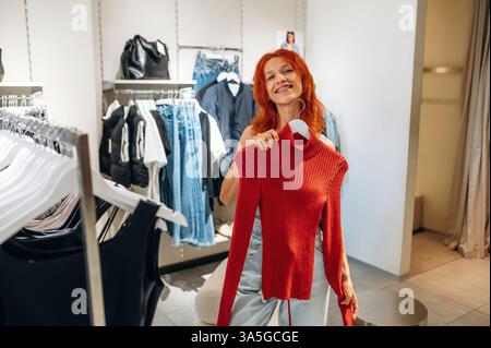 Maglione rosso. La donna sceglie i vestiti in un negozio. Foto Stock