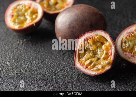 Frutti della passione e la sua sezione trasversale con succo polpato ripieno di semi su sfondo nero. Foto per striscioni orizzontali con spazio di copia Foto Stock