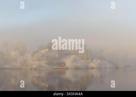 Calmo mare nebbia e gelo alla luce del mattino presto. Capanna e casa sulla spiaggia rossa. Vita sull'isola. Foto Stock