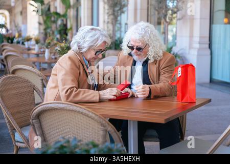 Felice coppia senior caucasica che si scambia un regalo in un caffè all'aperto momento gioioso. Foto Stock