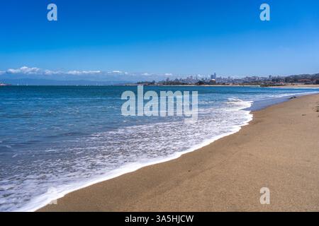 La spiaggia sabbiosa di Golden Gate Beach incontra l'Oceano Pacifico, con lo skyline di San Francisco visibile in lontananza sotto un cielo azzurro Foto Stock