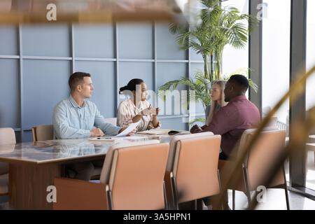 Team di professionisti che conduce discussioni formali seduti al banco conferenze in un ufficio moderno, impegnati nella condivisione degli aggiornamenti dei progetti, nella pianificazione della strategia o nel brai Foto Stock