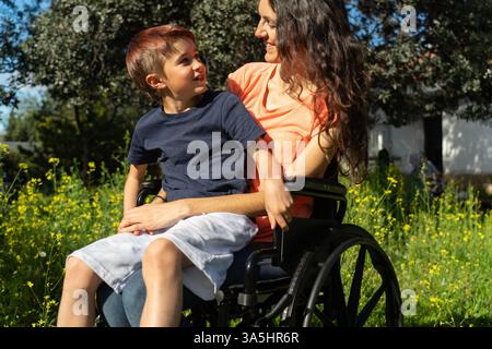 Scena emozionante di una madre disabile e suo figlio che trascorrono del tempo insieme in un parco soleggiato Foto Stock