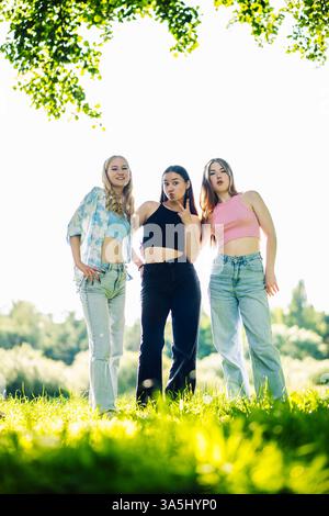 Amiche che ridono, scattano selfie durante il ritrovo all'aperto circondate dal verde del paesaggio Foto Stock