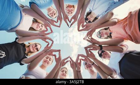 Gruppo di amici di scuola che formano una stella con le loro mani, simboleggiando l'unità, il lavoro di squadra e l'amicizia contro un cielo luminoso Foto Stock