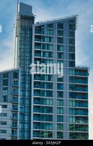 Un alto edificio con molte finestre e piccoli balconi si erge su un cielo blu con alcune nuvole a Manchester, Regno Unito. Foto Stock