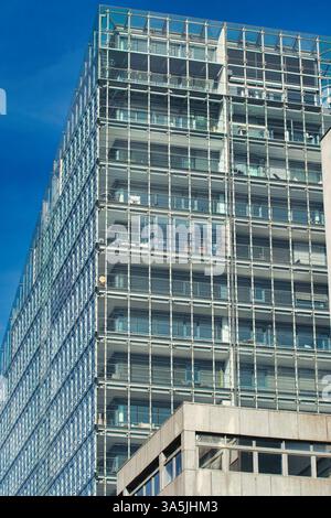 Una foto dall'angolo basso di un edificio moderno con una facciata in vetro, struttura simile a una griglia e sfondo blu cielo a Manchester, Regno Unito. Foto Stock